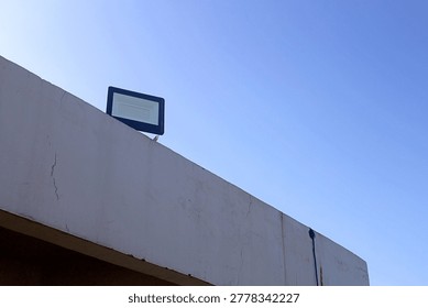Rectangular LED Floodlight on Weathered Concrete Wall against Clear Blue Sky