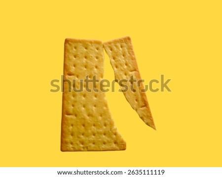 A rectangular, light-brown, perforated cracker is broken in half.The background is a solid, vibrant yellow.This image captures the simple elegance of everyday food items.