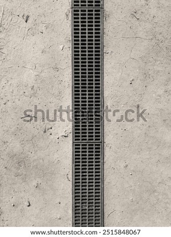 Rectangular metal drain grate set into a dry earth. There is a slight lip around the edge of the grate.	