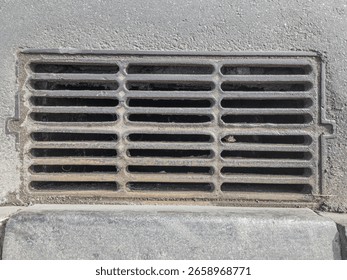 Rectangular metal storm drain grate embedded in asphalt pavement.