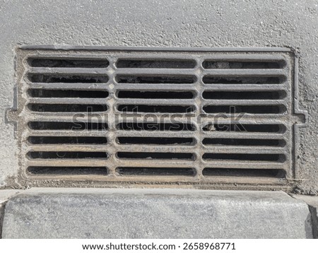 Rectangular metal storm drain grate embedded in asphalt pavement.