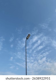 Rectangular modern street light facing a bright blue sky with scattered clouds. Tall, slender columns in a clean, minimalist outdoor scene, highlighting the simplicity of urban design