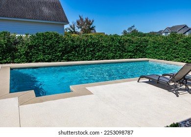 A rectangular new swimming pool with tan concrete edges in the fenced backyard of a new construction house. - Shutterstock ID 2253098787
