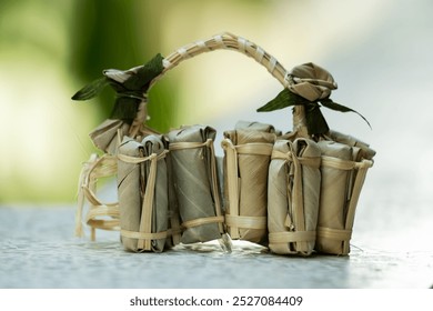 Rectangular objects are wrapped in white paper and then tied with bamboo strips. They are resting on a wooden surface, possibly a boardwalk. The objects appear to be a traditional Thai snack or treat.
