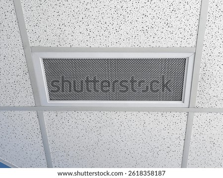 A rectangular, perforated metal grille, a Ventlab, installed in a suspended ceiling with a speckled pattern. The grille has a silver frame and centered within the ceiling tiles and support structure.