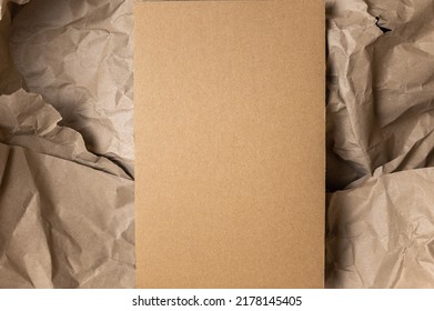 Rectangular piece of brown cardstock against crumpled wrapping paper. Copy space for text and design elements. Minimalist composition for various design tasks.  Top view.