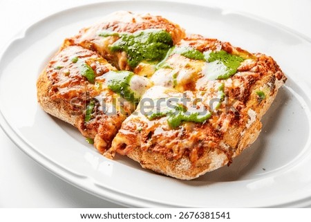 Rectangular pizza with thick rustic crust, melted cheese, tomato sauce, and green pesto, served on a white plate. Top-down view, gourmet style, vibrant colors
