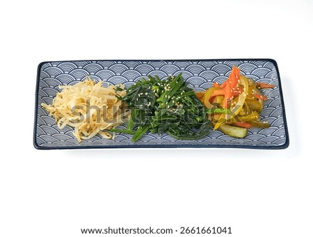 Rectangular plate with wave pattern holds three types of Korean vegetable side dishes seasoned bean sprouts, spinach, and pickled vegetables, garnished with sesame seeds