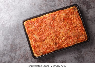 Rectangular Sfincione pizza with onions, tomatoes, cheese, anchovies and breadcrumbs closeup on a baking sheet on the table. Horizontal top view from above
