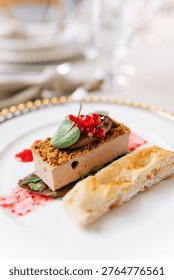 A rectangular slice of smooth pate topped with red currants and a green leaf, presented with a piece of flatbread and a berry coulis