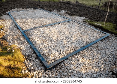 Rectangular steel frame on compacted crushed stone forms a level base in a yard. Metal edging and cross brace indicate DIY groundwork, with late day light and long shadows.