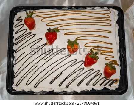 A rectangular strawberry cake covered with whipped cream, strawberries and caramel coulis
