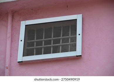 Rectangular Wall Vent with Metal Mesh Screen on Pink Textured Wall with Small Insects

Close-up of a rectangular ventilation opening covered with a protective metal mesh screen mounted on a textured pink plaster wall. The mesh surface shows several small insects resting on it while the cover is secured with visible fasteners along the edges. The vent allows airflow while preventing debris and pests from entering the interior space. This image represents home ventilation systems, wall vents, airflow management, building maintenance, and architectural details.