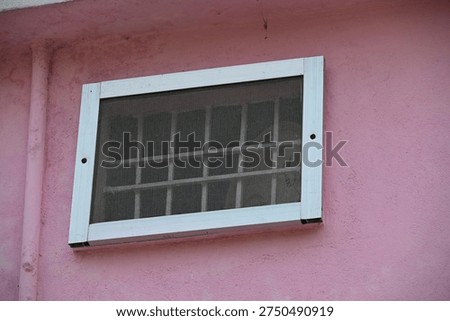 Rectangular Wall Vent with Metal Mesh Screen on Pink Textured Wall with Small Insects

Close-up of a rectangular ventilation opening covered with a protective metal mesh screen mounted on a textured pink plaster wall. The mesh surface shows several small insects resting on it while the cover is secured with visible fasteners along the edges. The vent allows airflow while preventing debris and pests from entering the interior space. This image represents home ventilation systems, wall vents, airflow management, building maintenance, and architectural details.