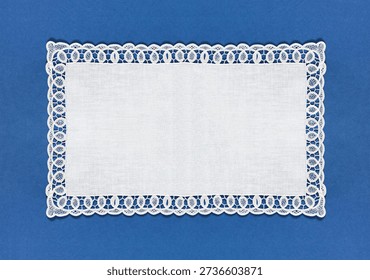 A rectangular white tablecloth with an openwork lace border on a blue background. Empty space for text. Close-up, top view, copy space, flat lay, collage, banner, mock up, blank