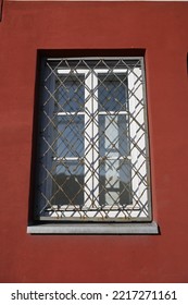 A Rectangular Window With Metal Bars In A Smooth Red Wall