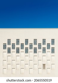 Rectangular windows and niches in the outer wall of the building against blue sky. Architectural elements repeating pattern of the modern built structure. Geometric exterior wall detail. Front view.