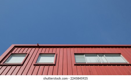 Rectangular windows on red corrugated facade against blue sky