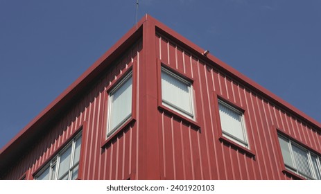 Rectangular windows on red corrugated facade against blue sky, facade corner