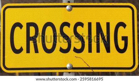 A rectangular yellow and black traffic sign that reads, Crossing. 