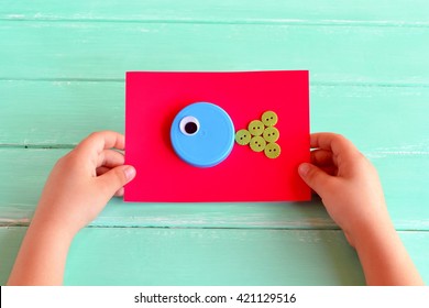 Recycle Bottle Caps Fish Crafts. Child Holding A Cardboard With Craft Fish. DIY Plastic Bottle Caps. Creative Bottle Cap Ideas. Recycle Crafts. Project To Make From Recycling Bottle Caps. Kids Art 