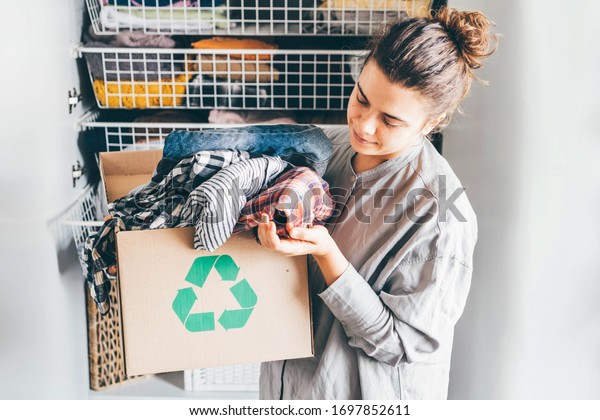 Recycle clothes concept. Young woman with\
recycling box full\
clothes.