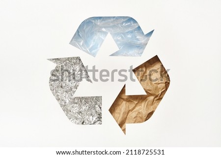 Recycle symbol made of cut paper with plastic, paper and foil on blue background. Reuse, reduce, recycle concept