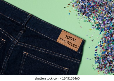 Recycled blue jeans with a clothing tag. Circular economy, zero waste concept. Reusing materials and reducing waste in fashion. Textile made from plastic waste. horizontal flat lay, green background