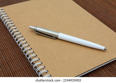 Recycled Note Book With White Pen On A Wooden Background. Concept School And Office Supplies.