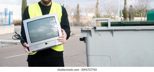 Recycling center worker holding an old tube television posing next to various dumpsters. Detail of a young man wearing a reflective vest. Concept of recycle electronics - Shutterstock ID 2092727743