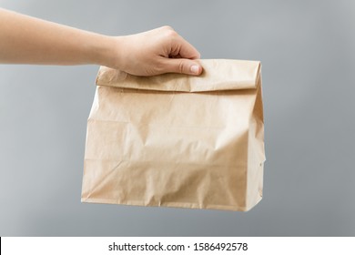 Recycling And Ecology Concept - Hand Holding Disposable Brown Takeaway Food In Paper Bag With Lunch On Table