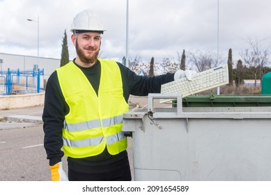 Recycling Plant Worker Throwing An Old Computer Keyboard To A Dumpster. Man Wearing Protective Gloves And Helmet And A Reflective Vest. Concept Of Recycle Electronics