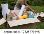 Recycling. Woman near cardboard box with different garbage outdoors, selective focus