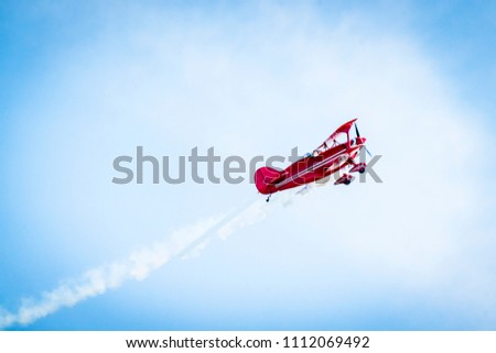 Red airplane with propellers and white smoke on the tail flying in the blue sky