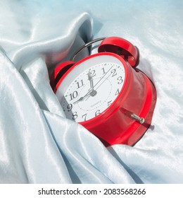 Red Alarm Clock In Blue Silk Sheets. Time Leisure Concept. Minimal Composition.