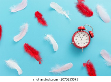 Red Alarm Clock And Feathers On Blue Background. No Hurry Concept. Good Mood. Relax And Weekend Concept. Time Leisure Concept.