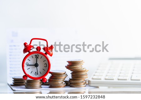Red alarm clock on stack of coins in concept of savings and money growing. Business investment growth concept. Retirement and Pension, Time passing concept.