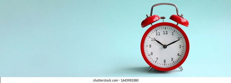 Red alarm clock on turquoise background shows 10 hours 10 minutes in evening or morning. Time to choice concept