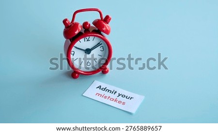 Red alarm clock with paper note advising to admit your mistakes