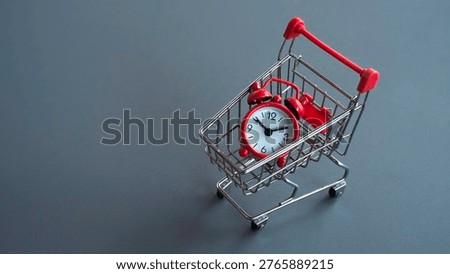 Red alarm clock placed inside a small silver shopping cart representing time-sensitive deals, limited time offers, and fast delivery service.