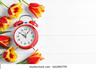 Red Alarm Clock, Spring Flowers And Space For Text On White Wooden Table, Flat Lay. Time Change