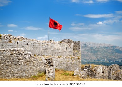 Red Albanian flag with double-headed black eagle waving over wall of Fortress Rozafa near Shkodra city. Fluttering banner with symbol of Albania on background of sky. Travel and tourism in Balkan
