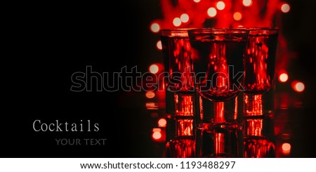 Red alcohol cocktails in shot glasses over red bokeh light and black background. Shots on bar counter in night club party.