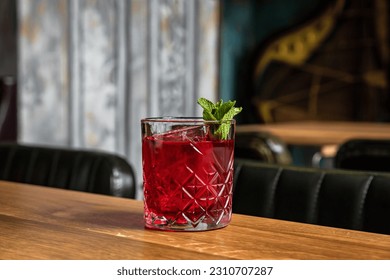 A red alcoholic cocktail in a rocks glass served on ice and garnished with mint on a wooden table in a restaurant or bar, horizontal photo - Powered by Shutterstock