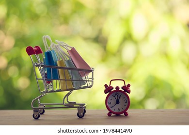 Red analog clock with shopping cart or a supermarket shopping basket and shopping bag on wood table. Fast delivery, time value of money concept : depicts the time is of the essence in our daily life. - Shutterstock ID 1978441490