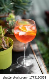 Red Aperol Spritz Cocktail Drink With Ice And Slice Of Orange On The Green Rooftop Garden Bar. Typical Refreshing Drink In Italy. Holiday - Party - Relax Concept Photo With Green Natural Background.