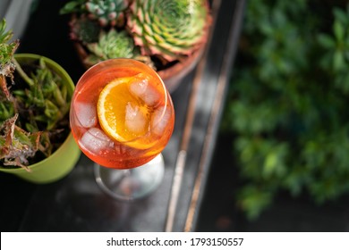 Red Aperol Spritz Cocktail Drink With Ice And Slice Of Orange On The Green Rooftop Garden Bar. Typical Refreshing Drink In Italy. Holiday - Party - Relax Concept Photo With Green Natural Background.