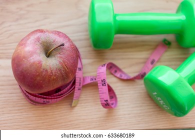 Red Apple Close Up With Green Dumb Bells And Measuring Tape. Diet And Work Out Concept Related