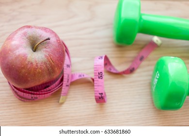 Red Apple Close Up With Green Dumb Bells And Measuring Tape. Diet And Work Out Concept Related