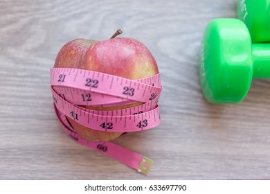 Red Apple Close Up With Green Dumb Bells And Measuring Tape. Diet And Work Out Concept Related